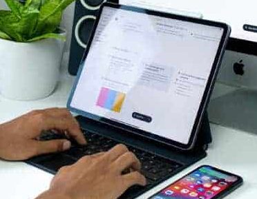A person using an iPad and a laptop on a desk