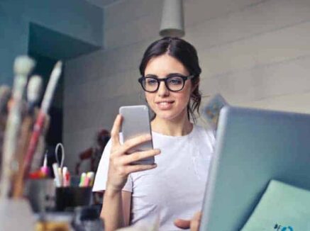A woman in glasses using her phone while sitting at a desk